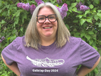 Profile Photo of Rachael Pozzo -Woman in a purple shirt smiling in front of lilacs