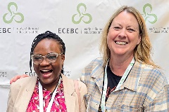 Two women stand in front of a backdrop with the ECEBC logo on it.